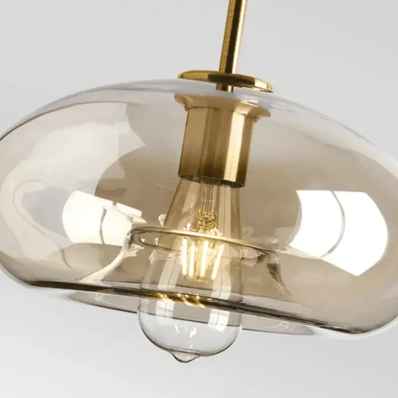 Detalhe do globo de vidro âmbar com encaixe dourado e lâmpada filamento E27 visível da luminária pendente industrial