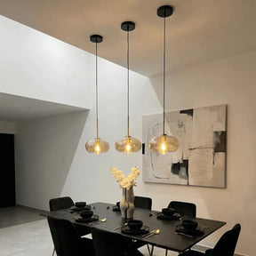 Três luminárias pendentes globo vidro âmbar sobre mesa de jantar preta em sala contemporânea com iluminação quente