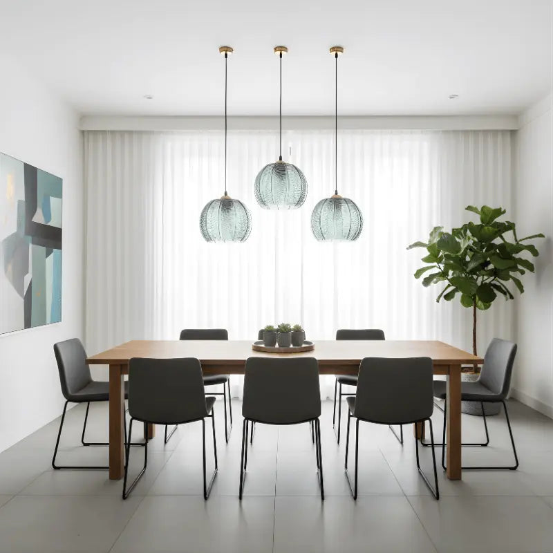 Três luminárias pendentes de vidro verde canelado sobre mesa retangular em sala de jantar minimalista com cortinas brancas