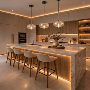 Luminárias pendentes globo vidro âmbar iluminando ilha de cozinha gourmet com bancada de mármore e banquetas brancas